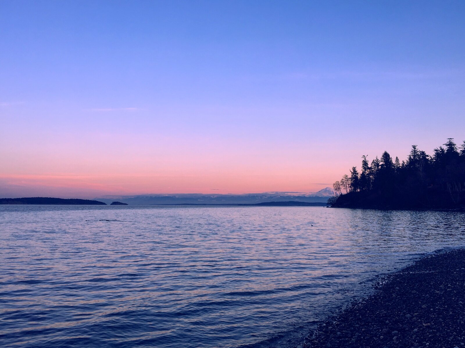 A dusk sky over calm water, with a distant mountain silhouette